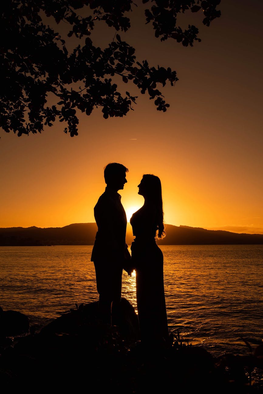 silhouette of man and woman standing near body of water